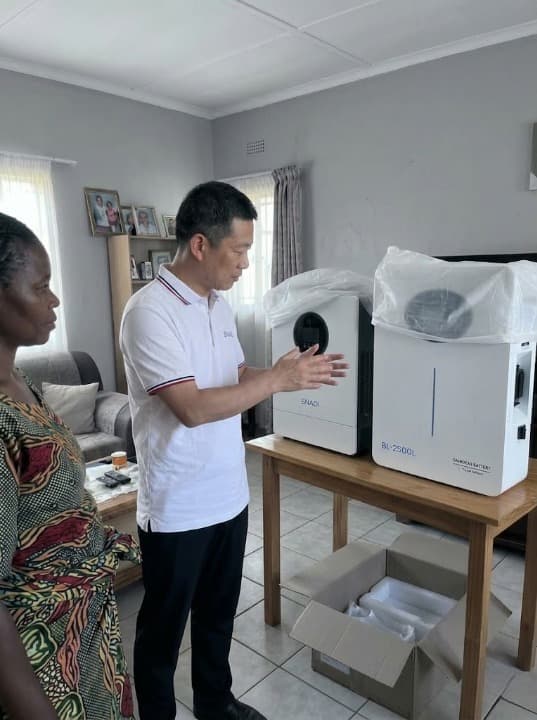 A SNADI Solar engineer in a white polo shirt demonstrating the BL-2500L lithium battery and solar inverter system to an African client in a home setting.